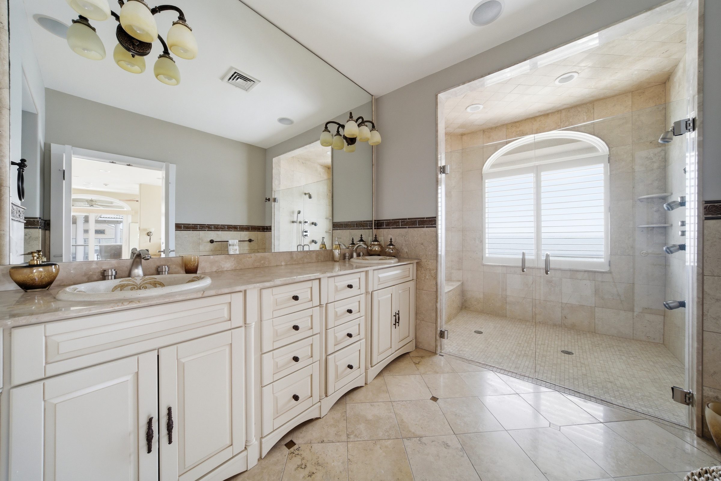 spa-inspired primary bathroom with dual sink vanity and glass-enclosed shower framed by a water-view window