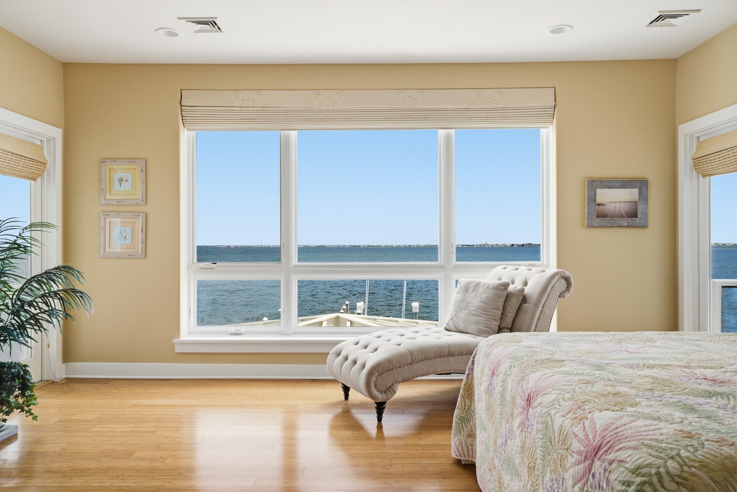 primary bedroom with tufted chaise and floor-to-ceiling windows overlooking the dock and water